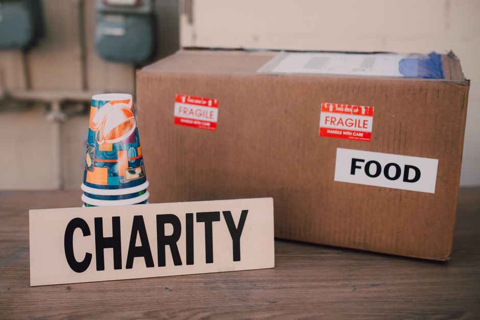 A cardboard box labeled 'FOOD' with red 'FRAGILE' stickers is placed on a wooden surface, alongside a stack of colorful disposable cups with a design featuring orange and blue elements. Next to the bo